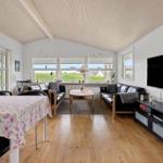 Wohn- und Essbereich mit Holzboden, schwarzen Sofas und TV. Fenster bieten Blick auf Grün.