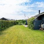Hinterhof mit Rasenfläche, Hecke und blauem Holzhaus. Gartenwerkzeug und Leiter sind vorhanden.