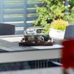 Ein Tisch mit Teekanne und Tassen auf einer Terrasse mit Stühlen und Pflanzen.