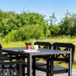Schwarzer Garten-Tisch mit vier Stühlen, Tasse und Pflanze vor grünem Hintergrund.