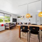 Wohn- und Essbereich mit Holzboden, Sofa, Esstisch und hängenden Lampen.