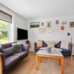 Wohnzimmer mit zwei Sofas, Holztisch und Wandbildern. Fenster mit Blick auf Grün.