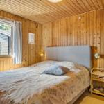 Schlafzimmer mit Holzwänden, Bett und Fensterblick auf eine Hütte.
