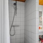 Badezimmer mit Dusche, Waschbecken und Spiegel. Holzdecke und weiße Fliesen.