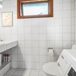 Badezimmer mit Waschbecken, Toilette und Waschmaschine. Weiße Fliesen und Holzfenster.
