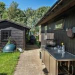 Außenküche mit Spüle und Hängeware an Holzhauswand. Neben einem Gartenhaus mit Gras und Pflanzen.