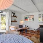 Wohnraum mit Sofa, Tisch und Blick auf Garten. Holzboden und weiße Wände.
