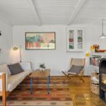 Wohnraum mit Sofa, Stuhl, Kamin und Wandbild. Holzboden und weiße Wände.
