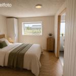 Schlafzimmer mit Bett, Kleiderschrank und Fenster. Holzfußboden und Türöffnung zum Badezimmer.