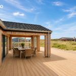 Holzterrasse mit Tisch und Stühlen unter Dach. Blick auf Dünen und Ferienhaus.
