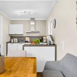 Kitchen with dining area and gray sofa. Wooden table, refrigerator, stove, and coffee machine.