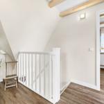 Attic with wooden floors, white railing, and chair. Window with curtains.