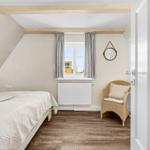 Bedroom with bed, wicker chair, and window with curtains.