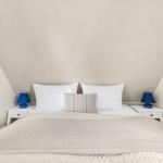 Bedroom with sloped ceiling, white bed, and two nightstands with blue lamps.