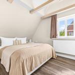 Bedroom with sloped ceiling, window, bed, and wooden floor.