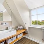 Bathroom with wooden washbasin, mirror, and window with view of green areas.