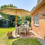 Terrace with table, chairs, and umbrella next to red brick house.