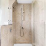 Shower with glass enclosure, beige tiles, and handheld shower.