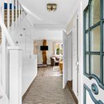 Hallway with staircase and view into living room with armchair and TV.