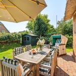 Terrace with table, chairs, and umbrella next to a red brick house.