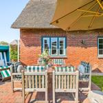 Terrace with table, chairs, and umbrella in front of a brick house with thatched roof.