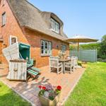 House with thatched roof, terrace with table, chairs, and umbrella.