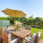 Wooden table with chairs and umbrella in the garden. Green lawn and hedge in the background.