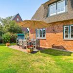 House with thatched roof and garden with table, chairs, and umbrella.