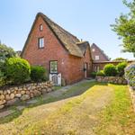 Red brick house with thatched roof, paved path, and stone walls with flower beds.
