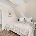 Bedroom with bed, nightstands, and wooden beams. Passage to stairs and wardrobe.