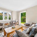 Living room with sofa, armchairs, table, and view of garden and street.