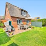 Red brick building with thatched roof and garden area with table, chairs, and umbrella.