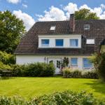 Haus mit Garten, Terrasse und Blumenbeete unter blauem Himmel.