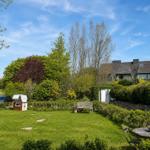 Haus mit Garten, Bäumen und einem Strandkorb. Holztisch und Stühle im Vordergrund.