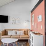 Wohnzimmer mit Sofa, Fernseher und Tisch. Wand in Rosa. Küche im Hintergrund.