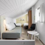 Schlafzimmer mit zwei Betten, Stuhl und Tisch unter schrägem Dach