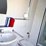 Badezimmer mit Dusche, Waschbecken und Toilette. Fliesenwand, Spiegel und Handtuchhalter.
