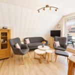 Wohnzimmer mit grauer Couch, zwei Sesseln und Holzmöbeln. Balkon mit Blick auf Dächer.