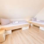 Zwei Einzelbetten mit Nachttischen und Lampen in einem Dachgeschosszimmer mit Holzboden.
