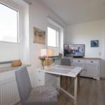 A room with a table, chairs, TV, and windows. Wooden floor and white furniture.