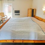 Ein Schlafzimmer mit großem Bett, Fernseher, Schrank und Stuhl vor Fenster.