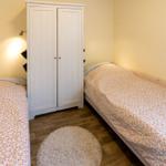 Zwei Betten mit Blumenbezug, weißer Schrank und runder Teppich im Raum.