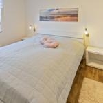 Schlafzimmer mit Bett, Fenster und Wandbild. Holzboden und zwei Nachttische.