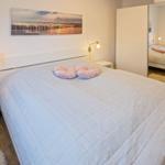 Schlafzimmer mit Bett, Nachttischen und Spiegelschrank. Wandbild über dem Bett.