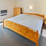 Schlafzimmer mit Holzbett, Kleiderschrank und Nachttisch. Tür zum Außenbereich.