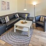 Ein Wohnzimmer mit schwarzer Ledercouch, weißem Tisch und Teppich auf Holzboden.