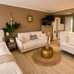Ein Wohnzimmer mit Sofa, Sessel und Bett. Holzboden und goldener Couchtisch.