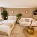 Schlafzimmer mit Sofa, Bett und Pflanzen. Holzboden und beige Wand.