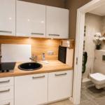 Küche mit weißen Schränken, Holz Arbeitsplatte und integriertem Spülbecken. Neben dem Bad mit Toilette.