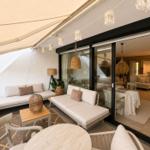 Terrasse mit Sitzgelegenheiten und Blick ins Haus. Glaswände und Hängelampen sichtbar.
